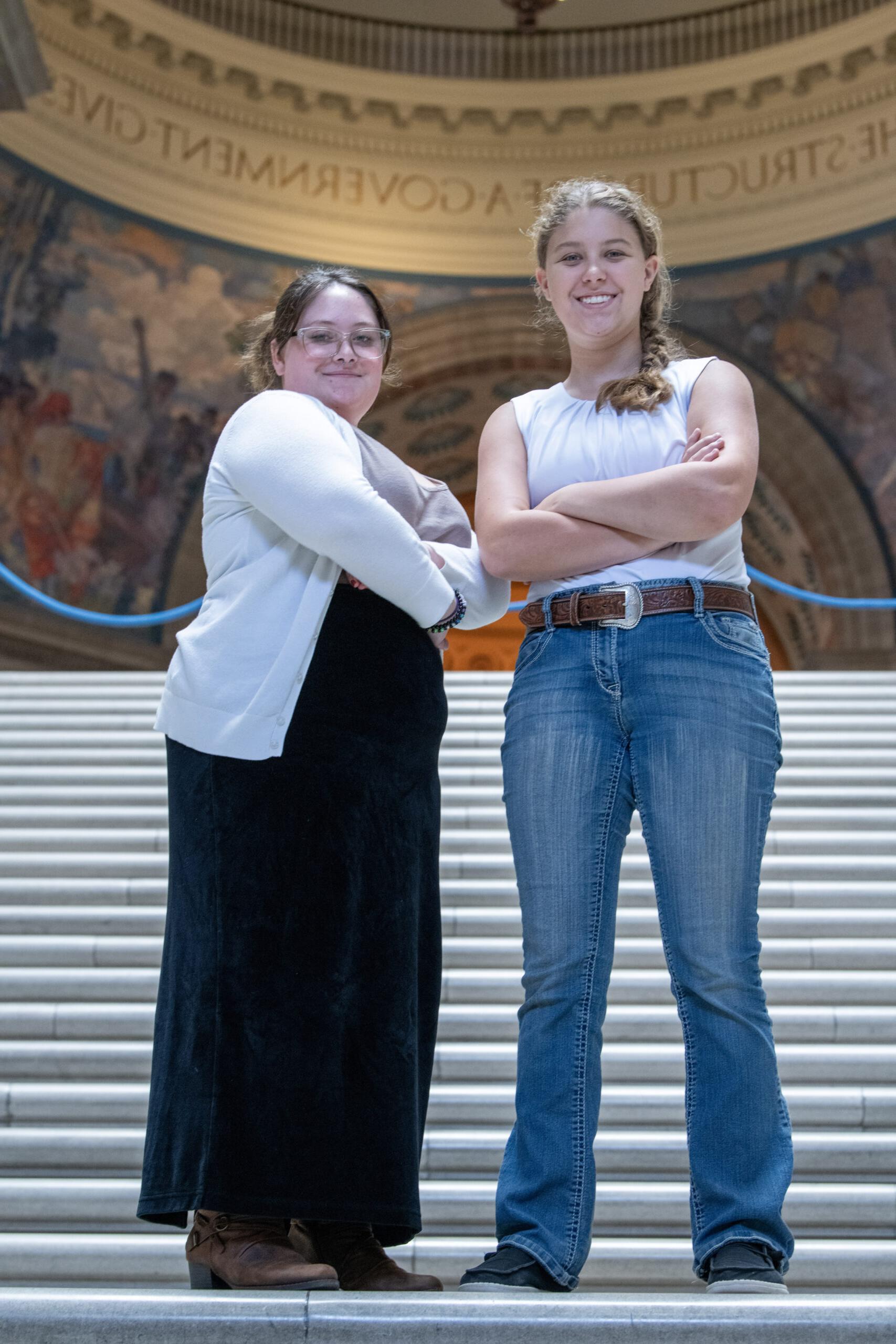 两名学生在政府大楼的台阶上双臂交叉摆姿势